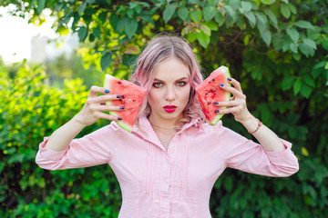 Beautiful young woman with pink hair holding two slices of watermelon in front of her face