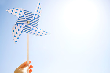 Handcrafted windmill pinwheel in kids' hand against the background of sky and sun