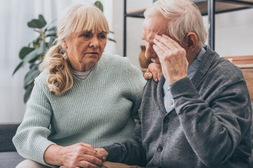 Wall Mural - retired woman holding hands with senior husband having headache