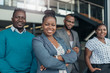 © JonoErasmus - Portrait of a confident black businesswoman crossing her arms smiling and looking into the camera with all african team in the background