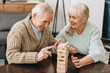 © LIGHTFIELD STUDIOS - cheerful retired husband and wife playing jenga game on table