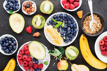 Wall Mural - Ingredients of a healthy breakfast: raspberries, blueberries, oat flakes, granola, honey, nuts, banana, avocado kiwi on the background Top View