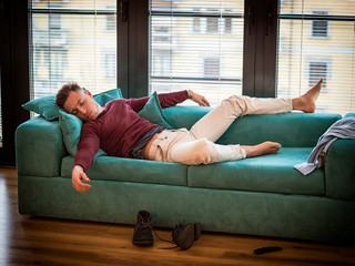 Drunk Young Handsome Man Resting on Couch in the Living Room with Head on the Floor.