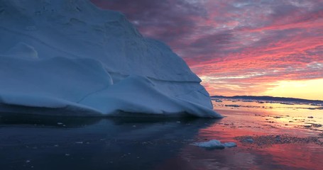Wall Mural - little red sailboat cruising among floating icebergs in disko bay glacier during midnight sun season