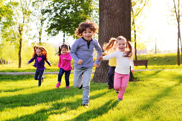 a group of small happy children run through the park in the background of grass and trees. Children's outdoor games, vacations, weekend, Children's Day, June 1