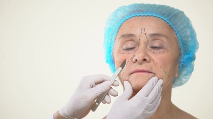 Wall Mural - Surgeon placing scalpel to aging female patient face with marks, face lifting