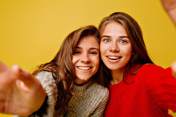 Two funny pretty girls with light-brown hairs and big eyes making selfie on bright yellow background, true emotions, happiness