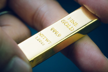 Hand holding gold bar as investment asset or safe haven on financial crisis, shinny ingot or bullion studio shot with dark background