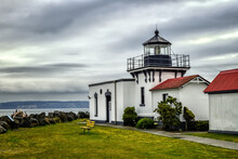 A Quaint Lighthouse Looks Out Over A Dramatic Sky And A Beautiful Body Of Water