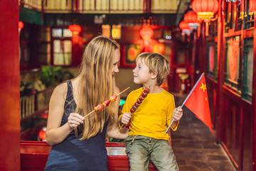 Wall Mural - Enjoying vacation in China. Happy tourists mom and son with a Chinese flag and with traditional Chinese candied fruits on a Chinese background. Travel to China with kids concept. Visa free transit 72