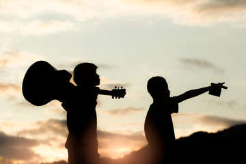 Wall Mural - Two young christian holding guitar on moutain with light sunset background,christian concept.