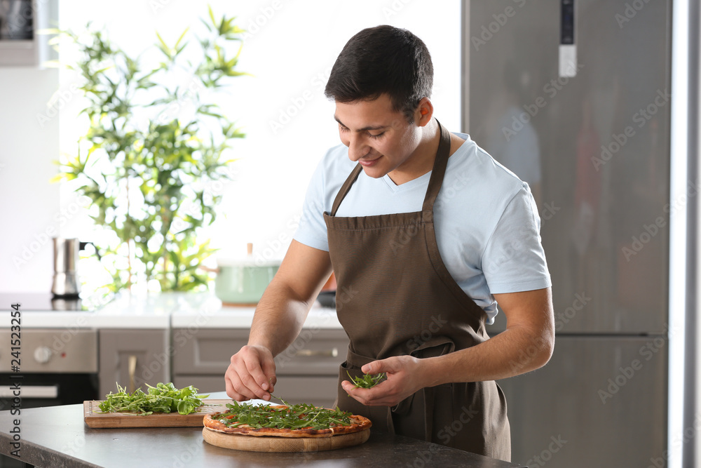 Young man decorating tasty pizza at table