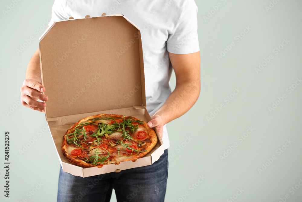 Young man holding box with tasty pizza on light background