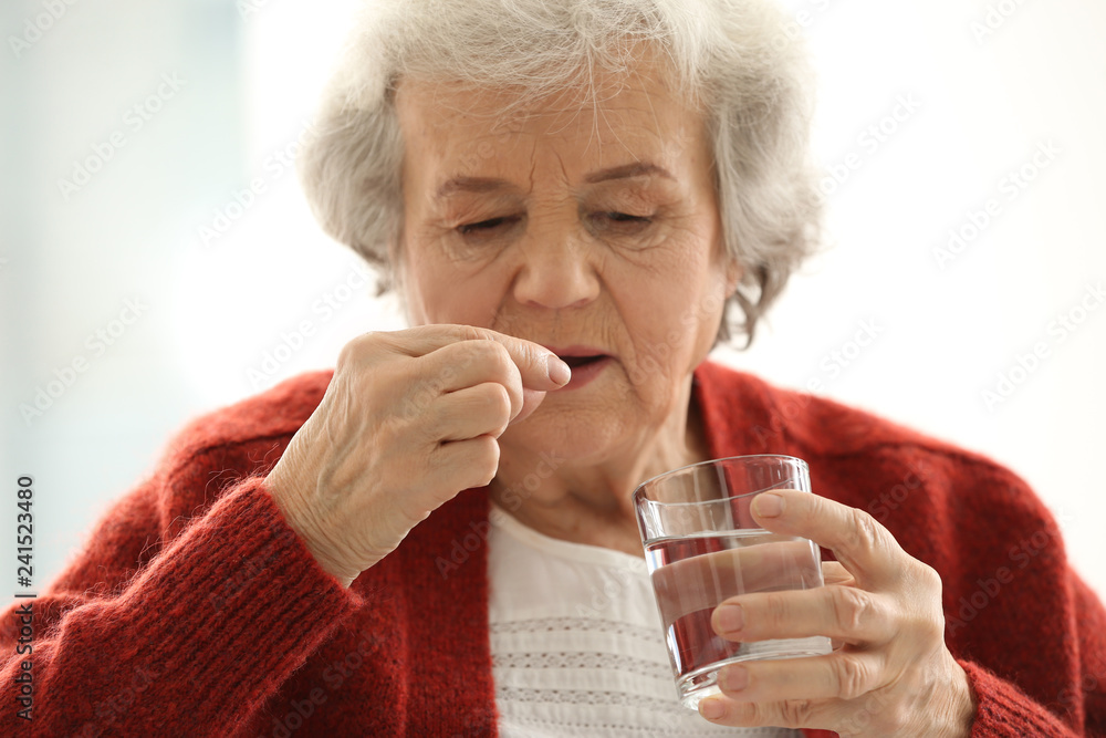 Elderly woman taking pill on light background