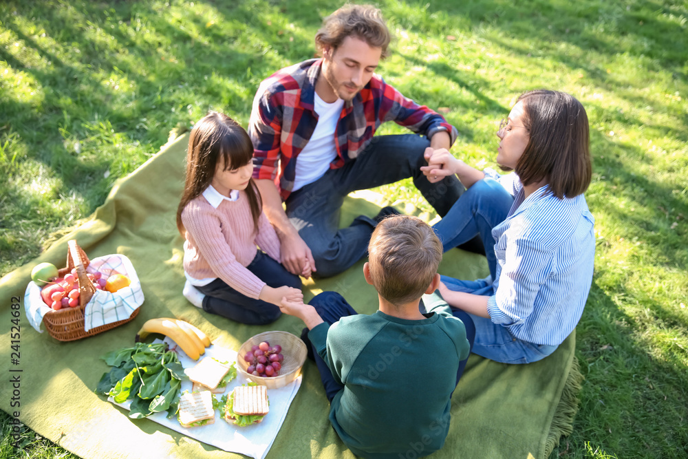 Family praying before meal in park