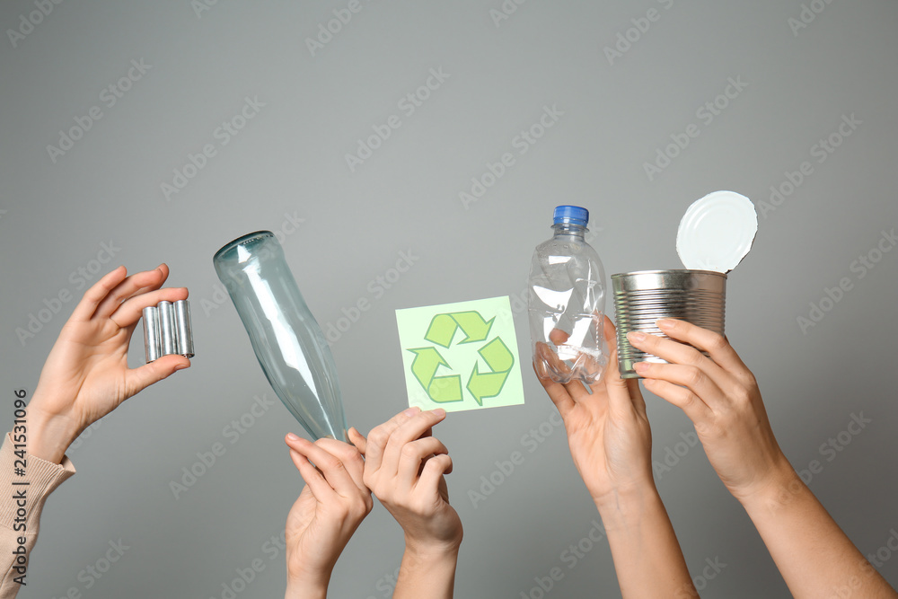 Many hands with different types of garbage and recycling symbol on grey background. Ecology concept