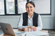 beautiful young kazakh businesswoman sitting at workplace and smiling at camera in office