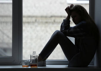 Wall Mural - Depressed woman drinking alcohol near window