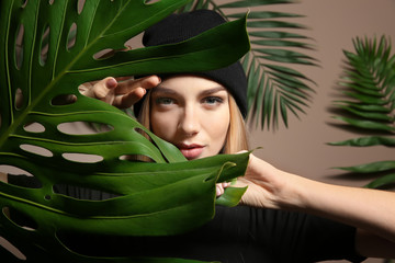 Wall Mural - Portrait of beautiful woman with green tropical leaves on color background