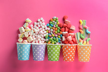 Paper Cups With Tasty Candies On Color Background