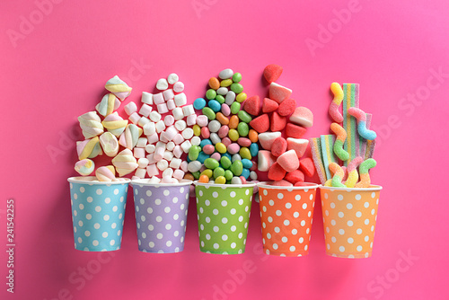 Fotomural Paper cups with tasty candies on color background