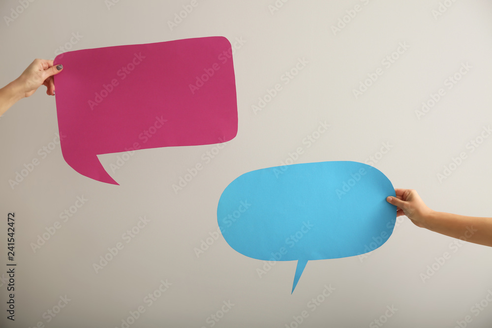 Female hands with blank speech bubbles on light background