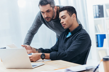 serious male coworkers working with papers and laptop in office