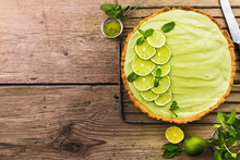 Key Lime Pie With Several Limes And Mint Over Wooden Background, Top View With Copy Space.