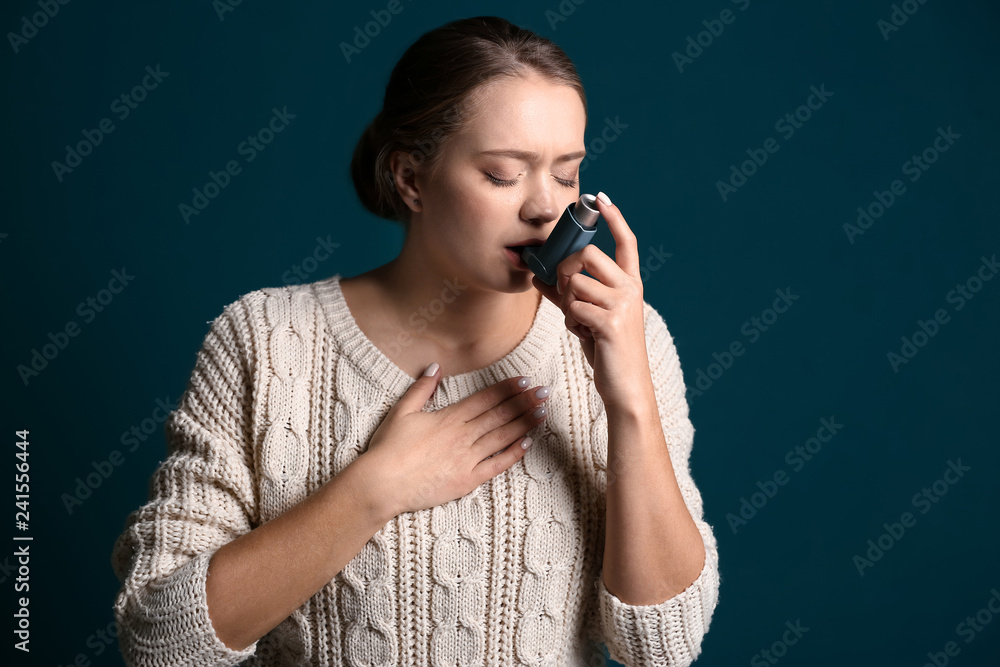 Young woman with inhaler having asthma attack on dark background
