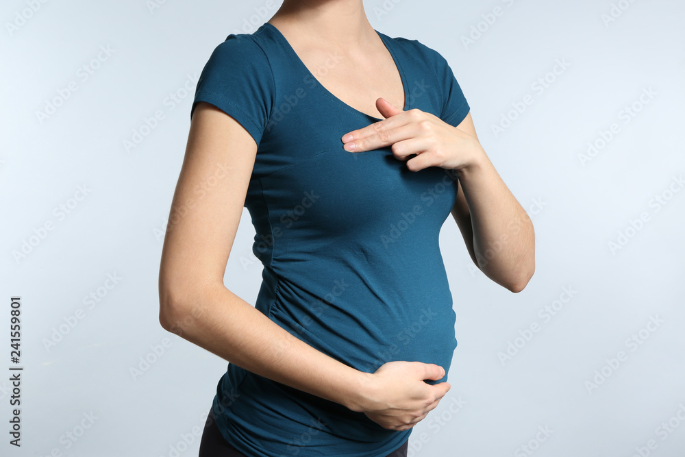Pregnant woman touching her breast on light background