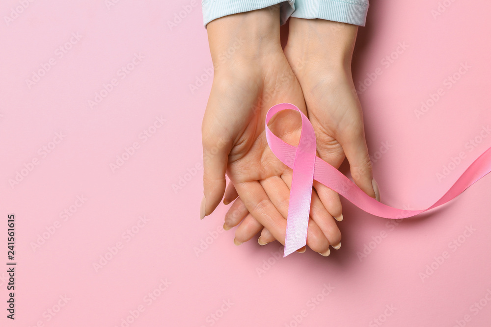 Female hands with pink ribbon on color background. Breast cancer awareness concept