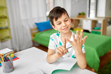 education, childhood and school concept - happy student boy counting using fingers at home