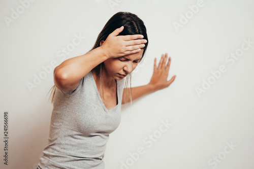 Woman suffering from dizziness with difficulty standing up while leaning on wall