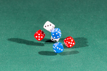 White, red and blue dices falling on a green table