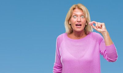 Canvas Print - Middle age blonde woman eatin pink macaron biscuit over isolated background scared in shock with a surprise face, afraid and excited with fear expression