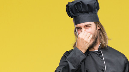 Young handsome cook man with long hair over isolated background smelling something stinky and disgusting, intolerable smell, holding breath with fingers on nose. Bad smells concept.