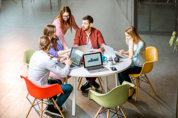 team of a young coworkers dressed casually working together with laptops sitting at the round table 
