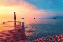 Silhouette Of A Child At Sunset Or Sunrise At The Sea In Greece Or Ocean On A Beach In Summer During Vacation. Freedom, Hope And Travel Destination Concept When Day Meets Night