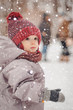 © Максим Галінский - Portrait of a cute baby dressed in a gray jacket and a red hat that walks through the snow covered park  enjoying first snow blowing