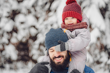 Wall Mural - Portrait of a happy man piggybacking his cheerful son or daughter. father and baby on winter holidays walking in a snowy park.