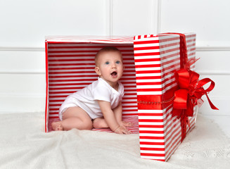 Infant child baby toddler kid sitting in big red presents gift box for celebration christmas 