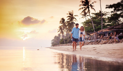 Wall Mural - Beautiful young love happy couple walking arm in arm on the beach at sunset during the honeymoon vacation travel