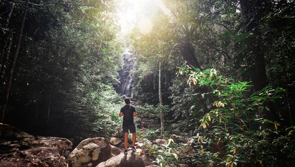 Handsome young stylish man in black t-shirt and sunglasses is engaged in trekking in the green jungle.