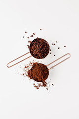 Rose gold measuring cups of cacao nips and cocoa powder on a white background, flat lay healthy food concept