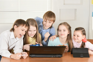 Wall Mural - Portrait of funny boys and girls playing computer game together at the table at home