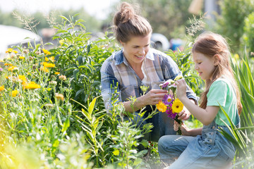 Smiling mother and daughter looking at flowers while gardening at farm