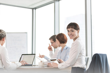 Portrait of smiling businesswoman sitting with colleagues in boardroom at office