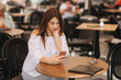 © Aleksandr - Young cheerful woman reading electronic book on smart phone, while waiting for her order