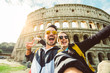 © Davide Angelini - Happy caucasian couple is taking a selfie smiling at the camera in front of the colosseum in Rome