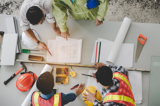 top view of group of engineer, technician and architect planning about building plan with blueprint and construction tools on the conference table at construction site, business and industry concept